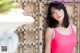 A woman in a pink tank top leaning against a wooden door.