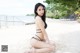 A woman in a black bikini sitting on a beach.