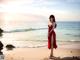 A woman in a red dress standing on a beach.